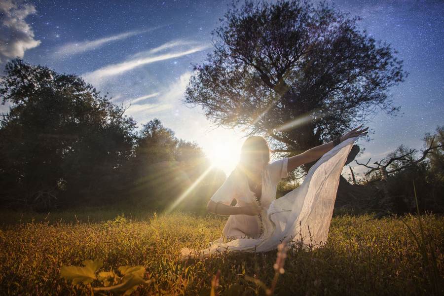 A figure sitting in an open field as the sun breaks through