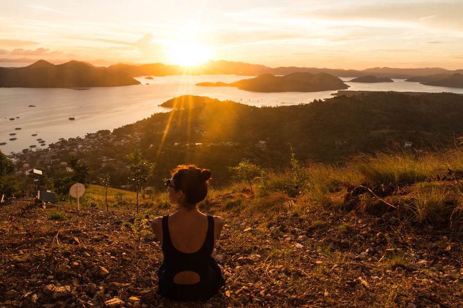 A woman sitting alone on a hilltop watching the sun come up over the water